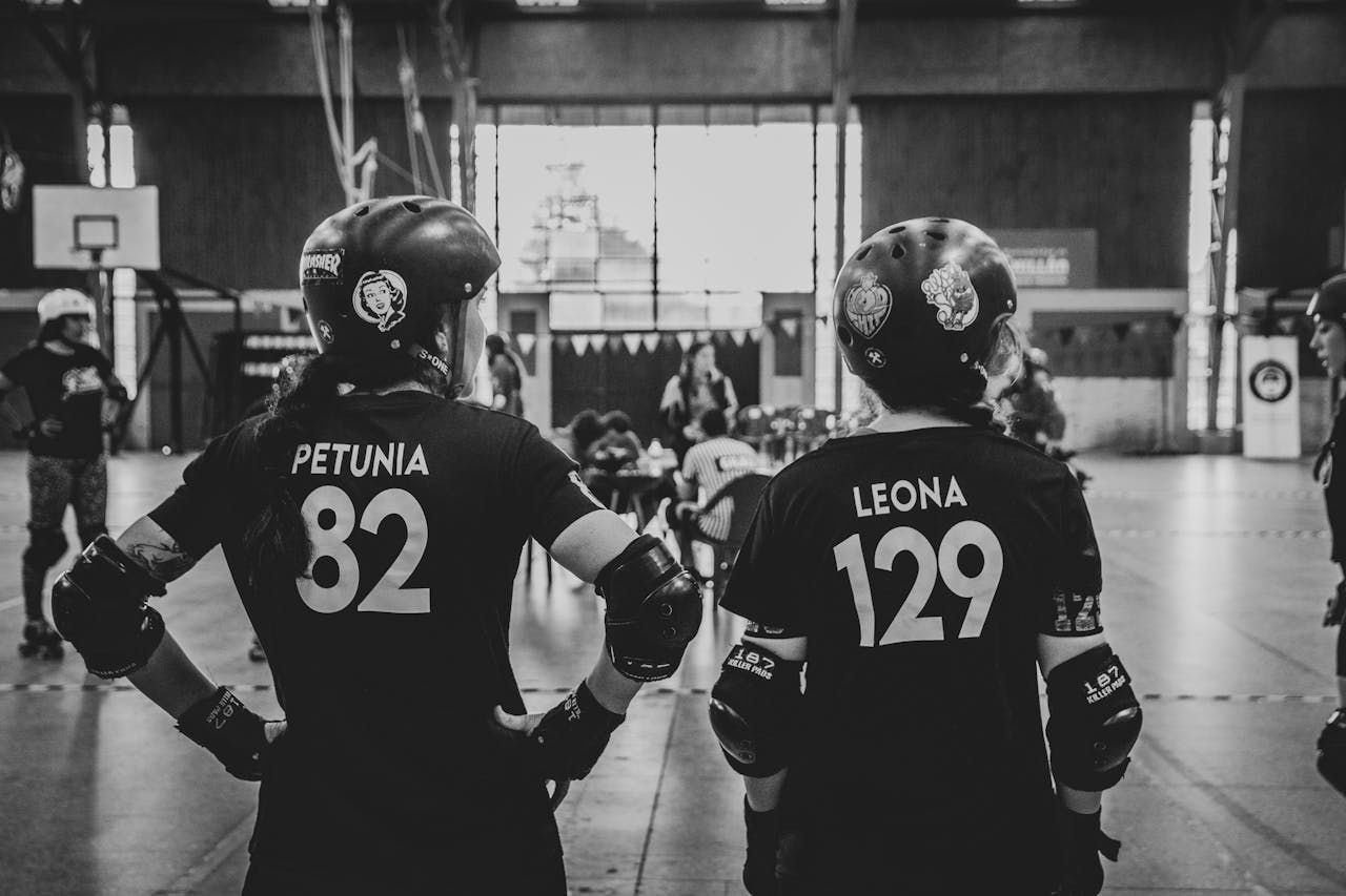 Black and white image of two roller derby women athletes standing in a skatepark wearing helmets and sportswear.
