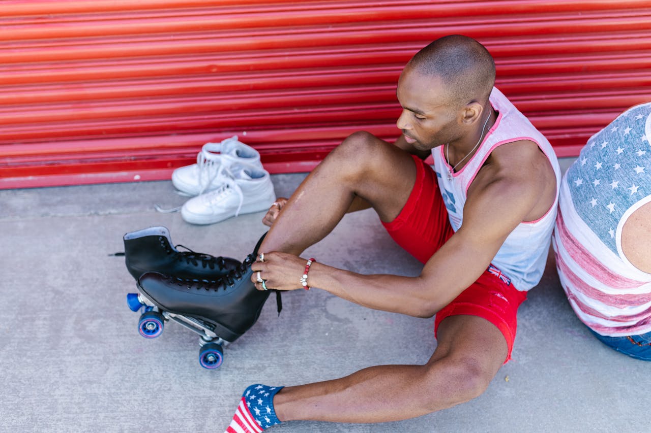 An adult man sits on the ground tying his roller skates, ready for an outdoor skate adventure.